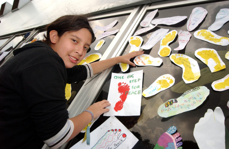 child with footprint images and a sign that says 'One Big Step For Peace'