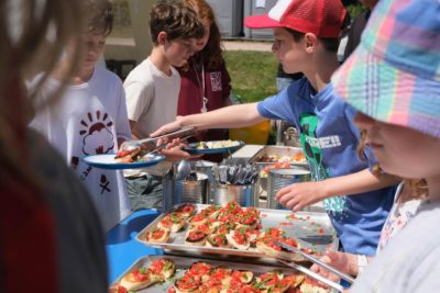 Six children standing around table serving bruschetta to each other while camping