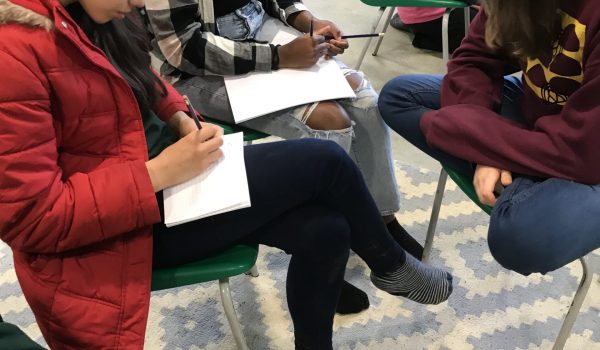 3 teenagers sitting on chairs making notes on paper